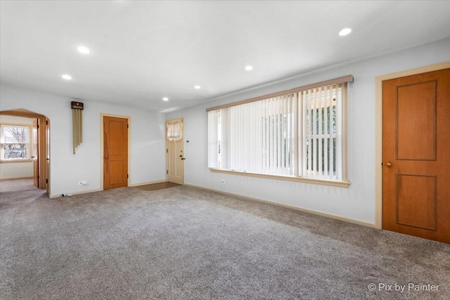 carpeted empty room featuring recessed lighting, arched walkways, and baseboards