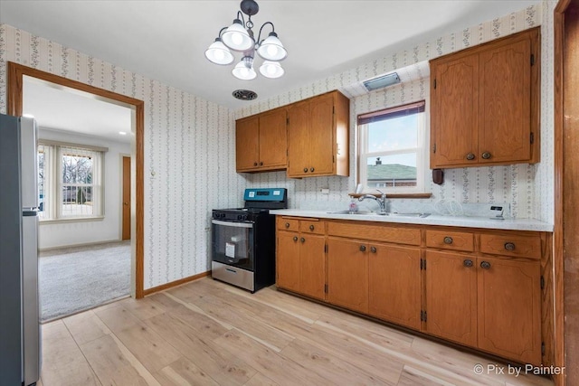 kitchen with light wood-style flooring, wallpapered walls, stainless steel appliances, and a sink