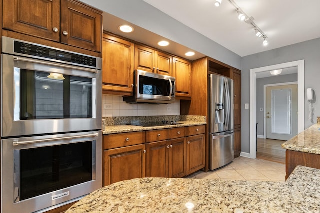 kitchen featuring light stone countertops, tasteful backsplash, appliances with stainless steel finishes, and brown cabinets