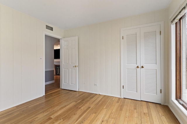 unfurnished bedroom with multiple windows, visible vents, light wood-type flooring, and a closet