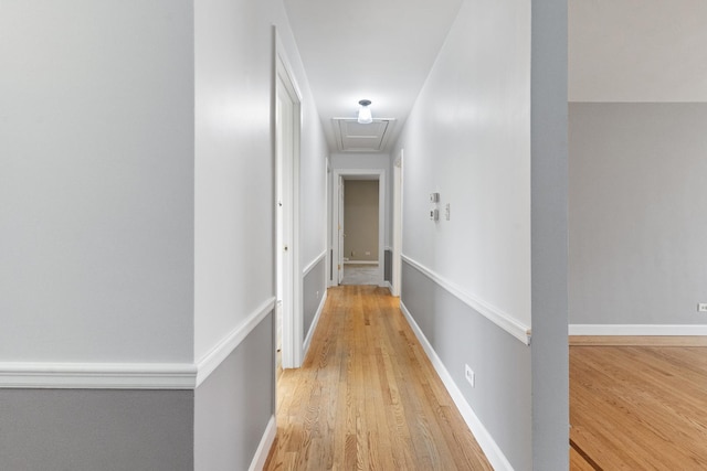 corridor featuring baseboards, attic access, and light wood finished floors