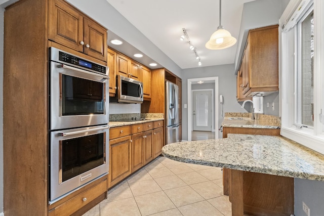 kitchen featuring a sink, light stone counters, appliances with stainless steel finishes, brown cabinetry, and light tile patterned floors