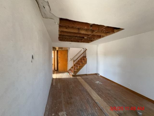 unfurnished living room with stairway, wood finished floors, and baseboards