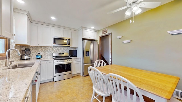 kitchen with a ceiling fan, a sink, tasteful backsplash, appliances with stainless steel finishes, and white cabinets