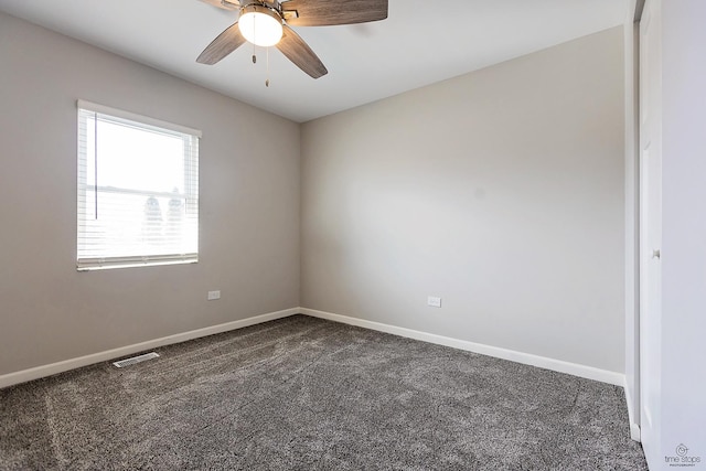 spare room with visible vents, ceiling fan, baseboards, and dark colored carpet