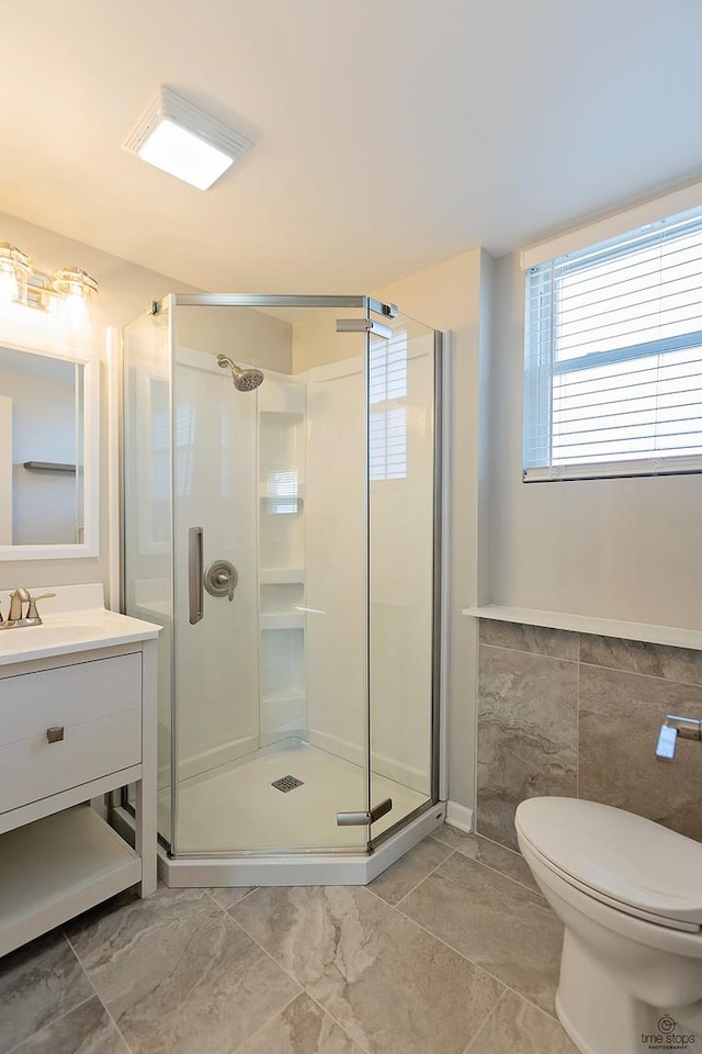 full bathroom featuring a shower stall, tile walls, a wainscoted wall, toilet, and vanity