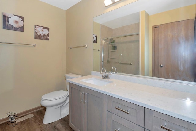 bathroom featuring toilet, wood finished floors, a shower stall, baseboards, and vanity