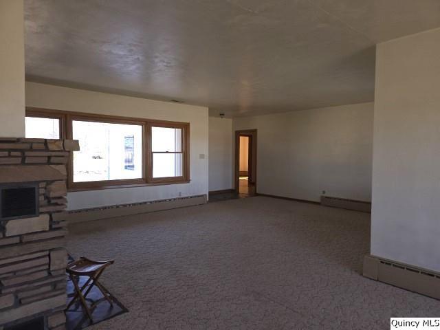 unfurnished living room featuring a baseboard heating unit, baseboard heating, a fireplace, and carpet