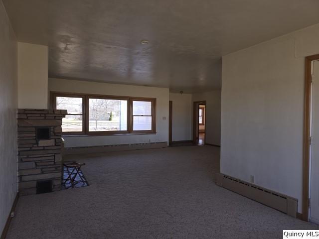 unfurnished living room featuring a stone fireplace, carpet flooring, and a baseboard radiator