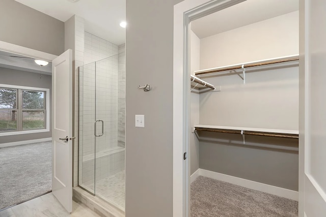 full bathroom featuring a spacious closet, a shower stall, and baseboards