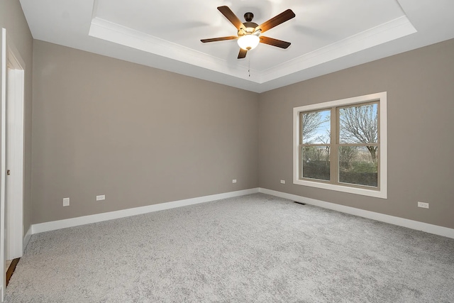 carpeted empty room featuring a tray ceiling, crown molding, a ceiling fan, and baseboards