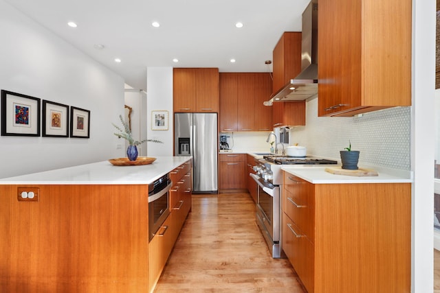 kitchen with a sink, stainless steel appliances, light countertops, wall chimney range hood, and brown cabinets