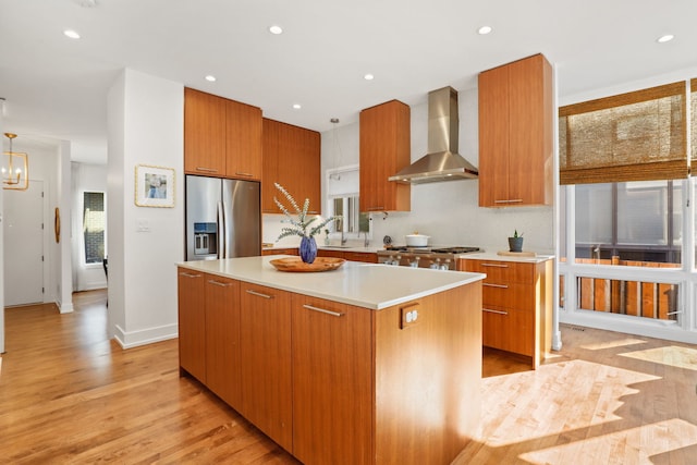 kitchen featuring modern cabinets, a kitchen island, stainless steel fridge, wall chimney exhaust hood, and stove