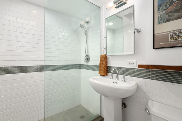 full bath featuring a tile shower, toilet, tile walls, and a sink