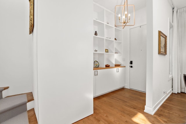 hallway featuring light wood-type flooring, baseboards, and an inviting chandelier