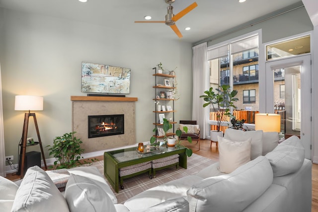 living area with a glass covered fireplace, recessed lighting, a ceiling fan, and wood finished floors