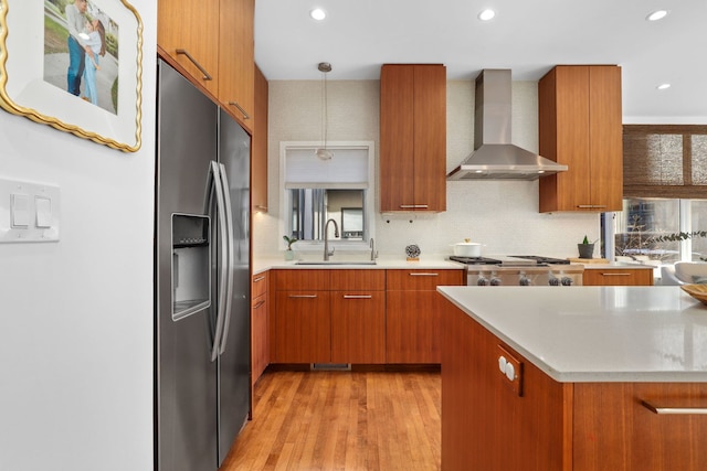 kitchen with brown cabinets, stove, stainless steel fridge, wall chimney exhaust hood, and a sink