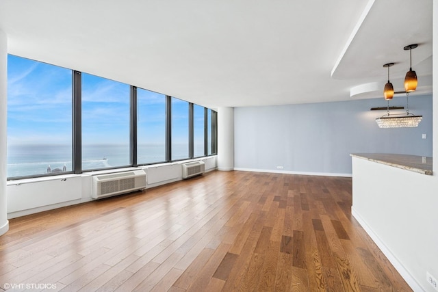 unfurnished living room with a wall unit AC, wood finished floors, baseboards, a wall mounted AC, and a water view