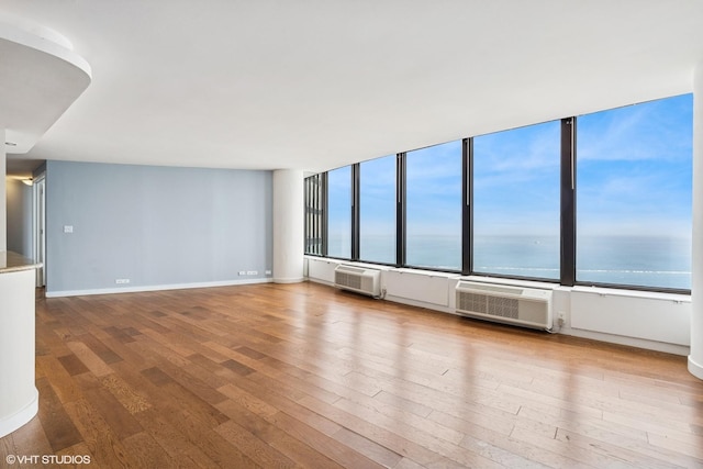 empty room with a water view, an AC wall unit, wood finished floors, and a healthy amount of sunlight