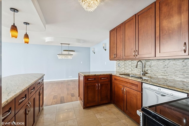 kitchen featuring a sink, backsplash, a peninsula, light stone countertops, and hanging light fixtures