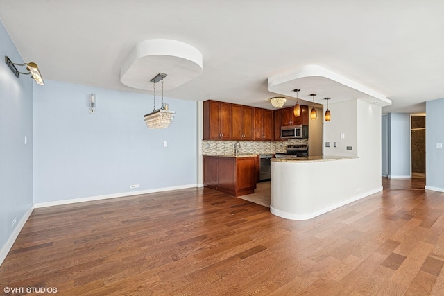 kitchen featuring backsplash, pendant lighting, wood finished floors, brown cabinetry, and stainless steel appliances