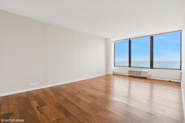 empty room featuring baseboards, wood finished floors, and a wall unit AC