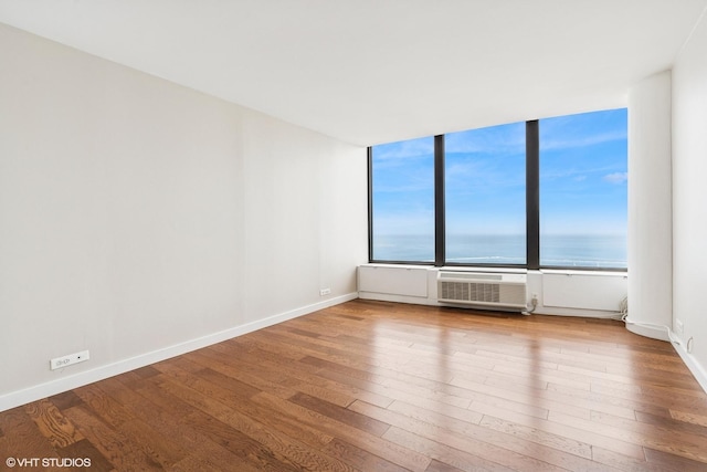 unfurnished room featuring wood finished floors, baseboards, and a water view