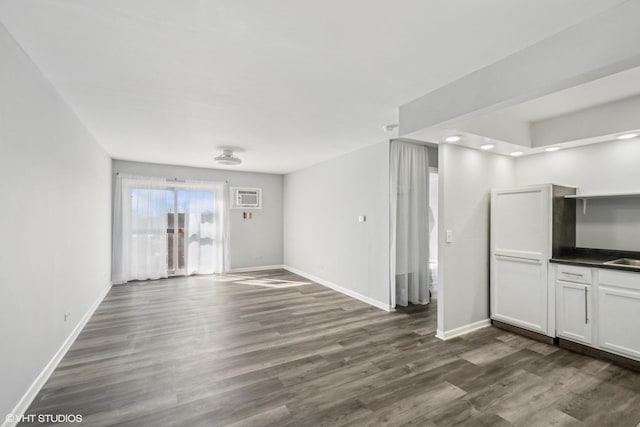 unfurnished living room with dark wood finished floors, an AC wall unit, and baseboards