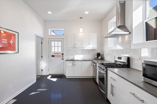 kitchen featuring pendant lighting, backsplash, appliances with stainless steel finishes, white cabinets, and wall chimney range hood