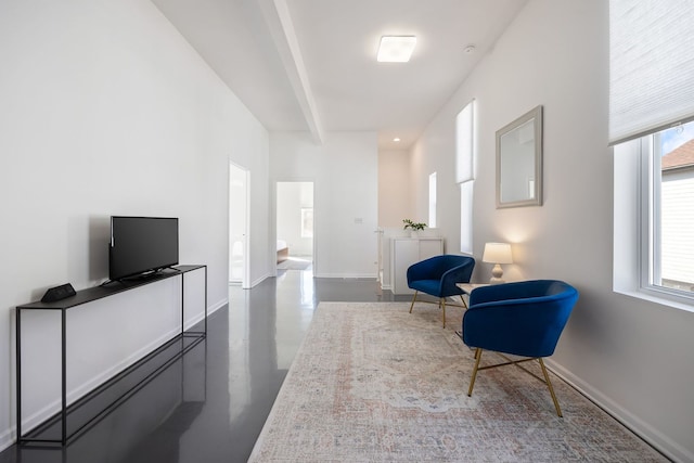 living area with beamed ceiling, finished concrete flooring, and baseboards