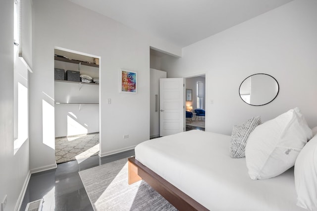 bedroom featuring visible vents, baseboards, finished concrete floors, a spacious closet, and a closet