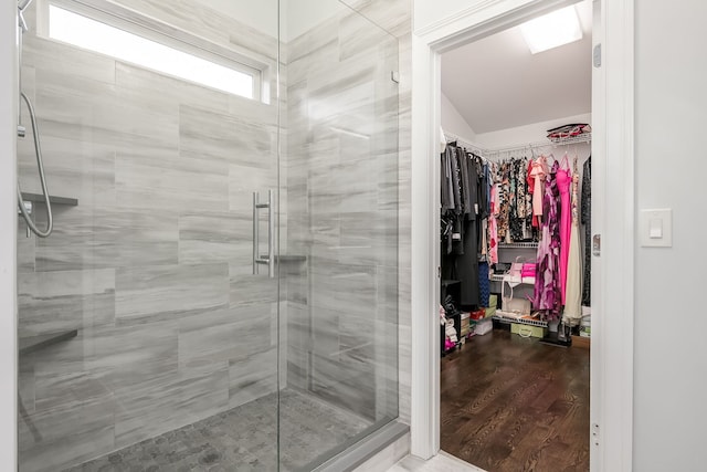 bathroom with a walk in closet, wood finished floors, and a stall shower