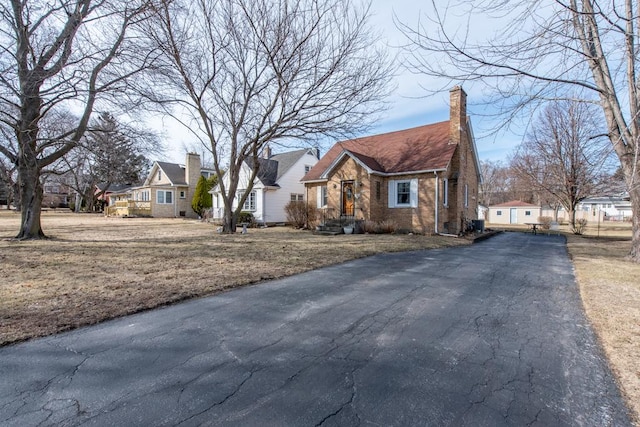 view of front of house with aphalt driveway, a chimney, and brick siding