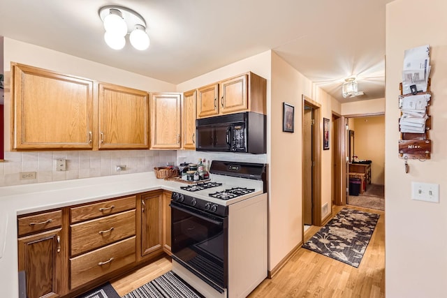 kitchen with light wood finished floors, backsplash, black microwave, light countertops, and range with gas stovetop