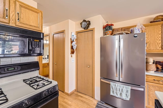 kitchen featuring light wood finished floors, white range with gas stovetop, freestanding refrigerator, light countertops, and black microwave