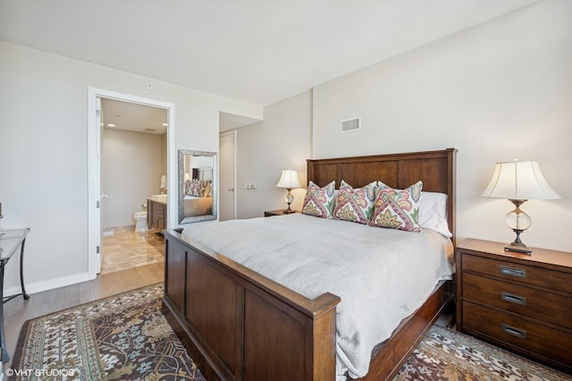 bedroom with wood finished floors, visible vents, and ensuite bathroom