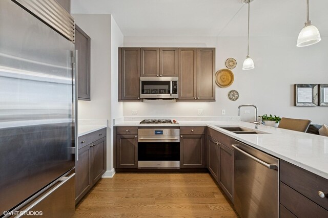 kitchen with a sink, hanging light fixtures, light countertops, appliances with stainless steel finishes, and light wood-type flooring