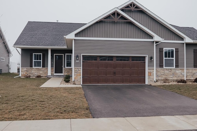 craftsman house with a front lawn, an attached garage, stone siding, and a shingled roof