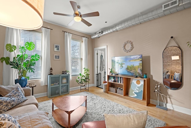 living room featuring ceiling fan, visible vents, baseboards, and wood finished floors