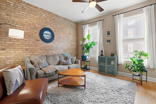 living area featuring wood finished floors, baseboards, brick wall, and ceiling fan