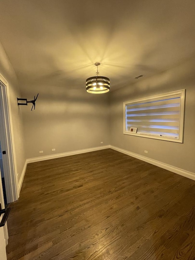 empty room featuring visible vents, dark wood-style flooring, and baseboards