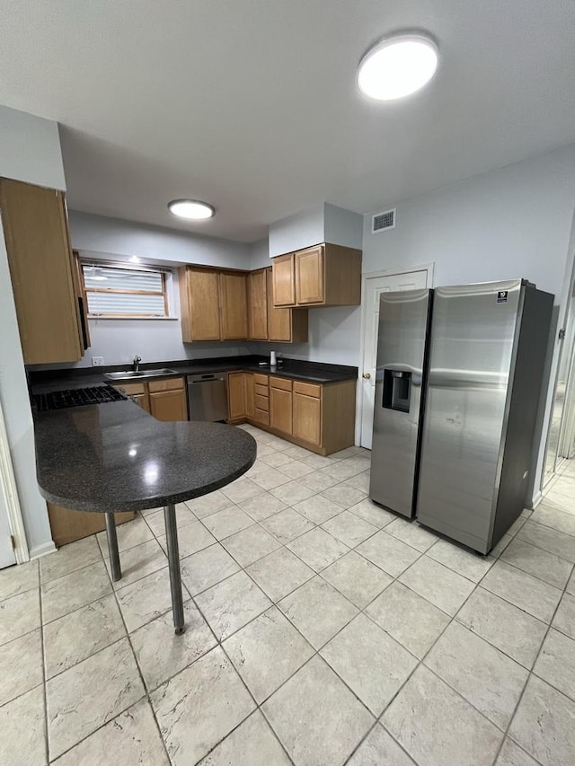 kitchen with visible vents, a sink, dark countertops, stainless steel appliances, and brown cabinetry