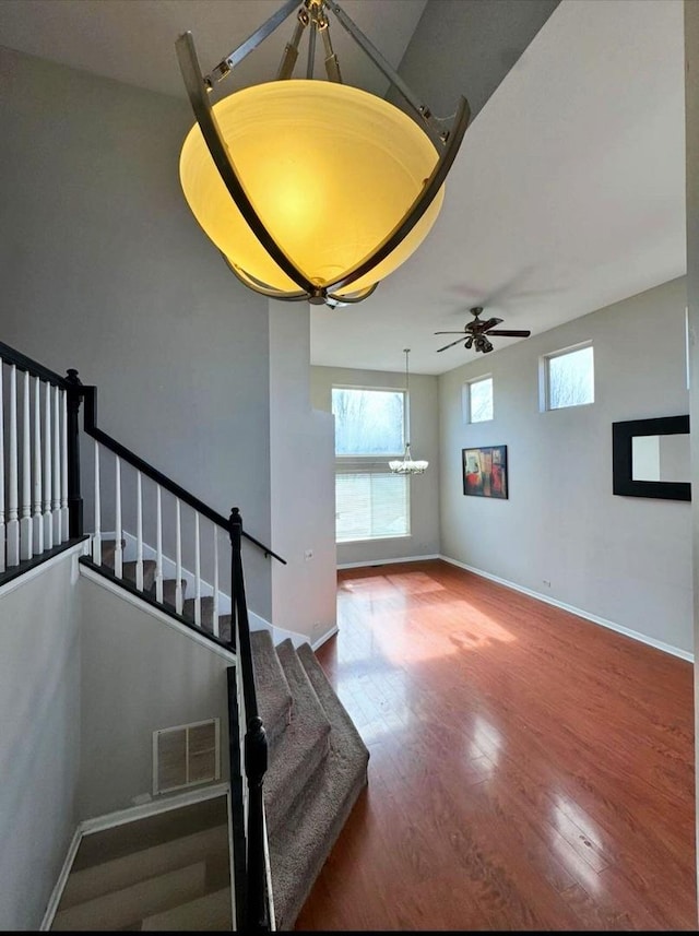 staircase featuring visible vents, ceiling fan with notable chandelier, baseboards, and wood finished floors