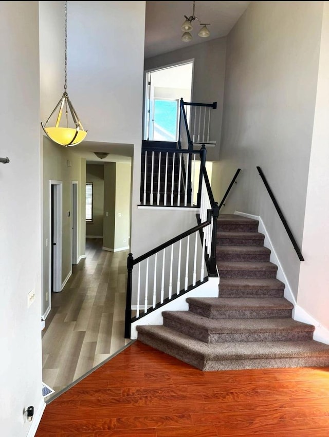 staircase featuring a wealth of natural light, a high ceiling, baseboards, and wood finished floors