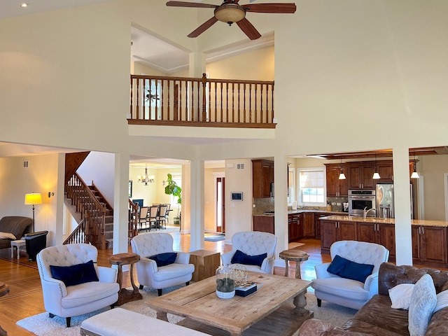 living area featuring stairway, light wood-style floors, a towering ceiling, and ceiling fan with notable chandelier