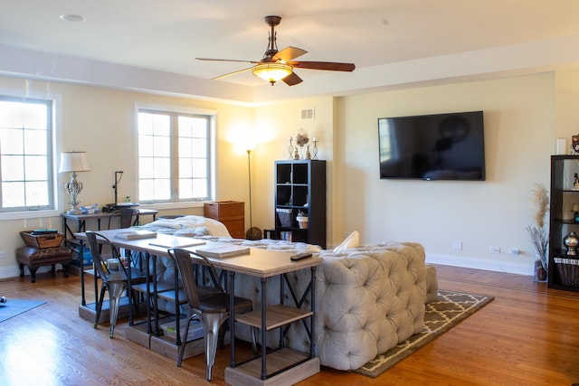living area with a wealth of natural light, visible vents, wood finished floors, and ceiling fan