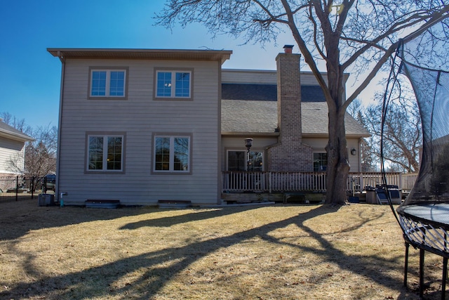 back of property with a trampoline, fence, a yard, a wooden deck, and a chimney