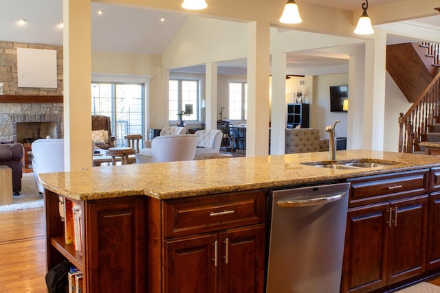 kitchen with a sink, light stone counters, open floor plan, a fireplace, and dishwasher
