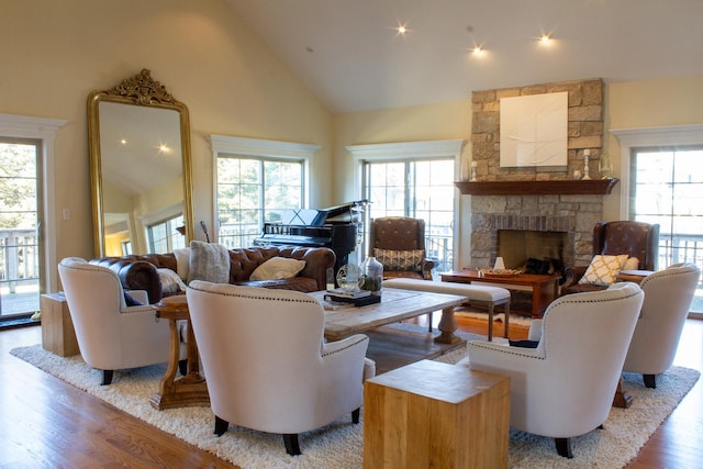 living room with a stone fireplace, wood finished floors, and high vaulted ceiling