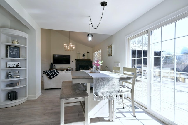 dining space featuring built in features, lofted ceiling, light wood-style floors, a brick fireplace, and a chandelier